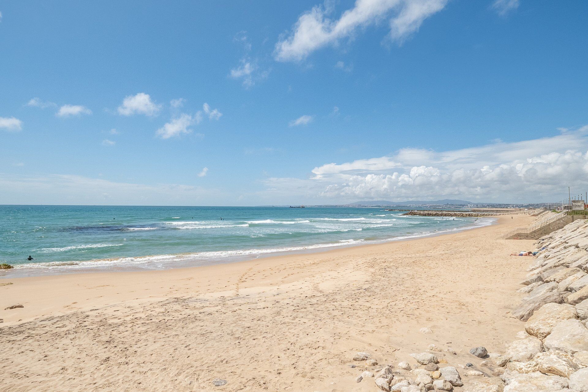 Uma praia com costa rochosa, mar calmo e céu claro.