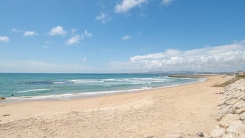 Uma praia com costa rochosa, mar calmo e céu claro.