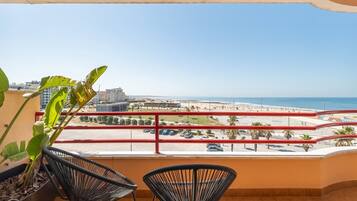 Un balcon avec deux chaises, une vue sur la plage et un espace de stationnement.