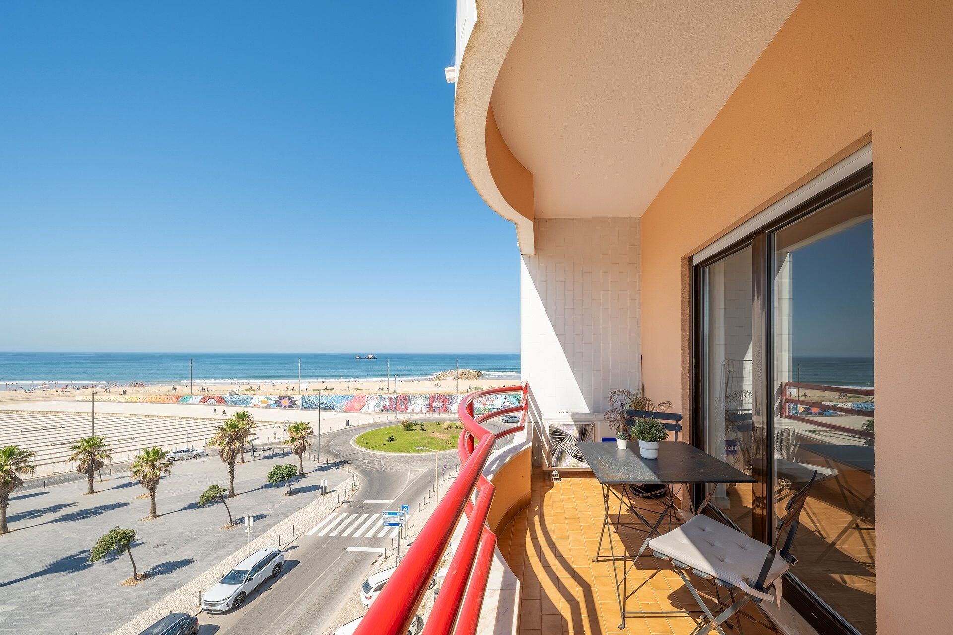 Een balkon met uitzicht op het strand, een tafel met stoelen en een bloempot.