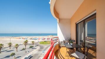Een balkon met uitzicht op het strand, een tafel met stoelen en een bloempot.