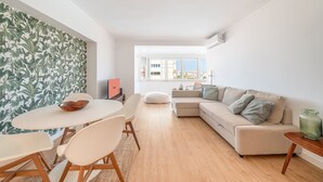 A modern living space with a dining area, a sofa, and a view of the city. - GuestReady - Stay at Costa da Caparica (Costa de Caparica)