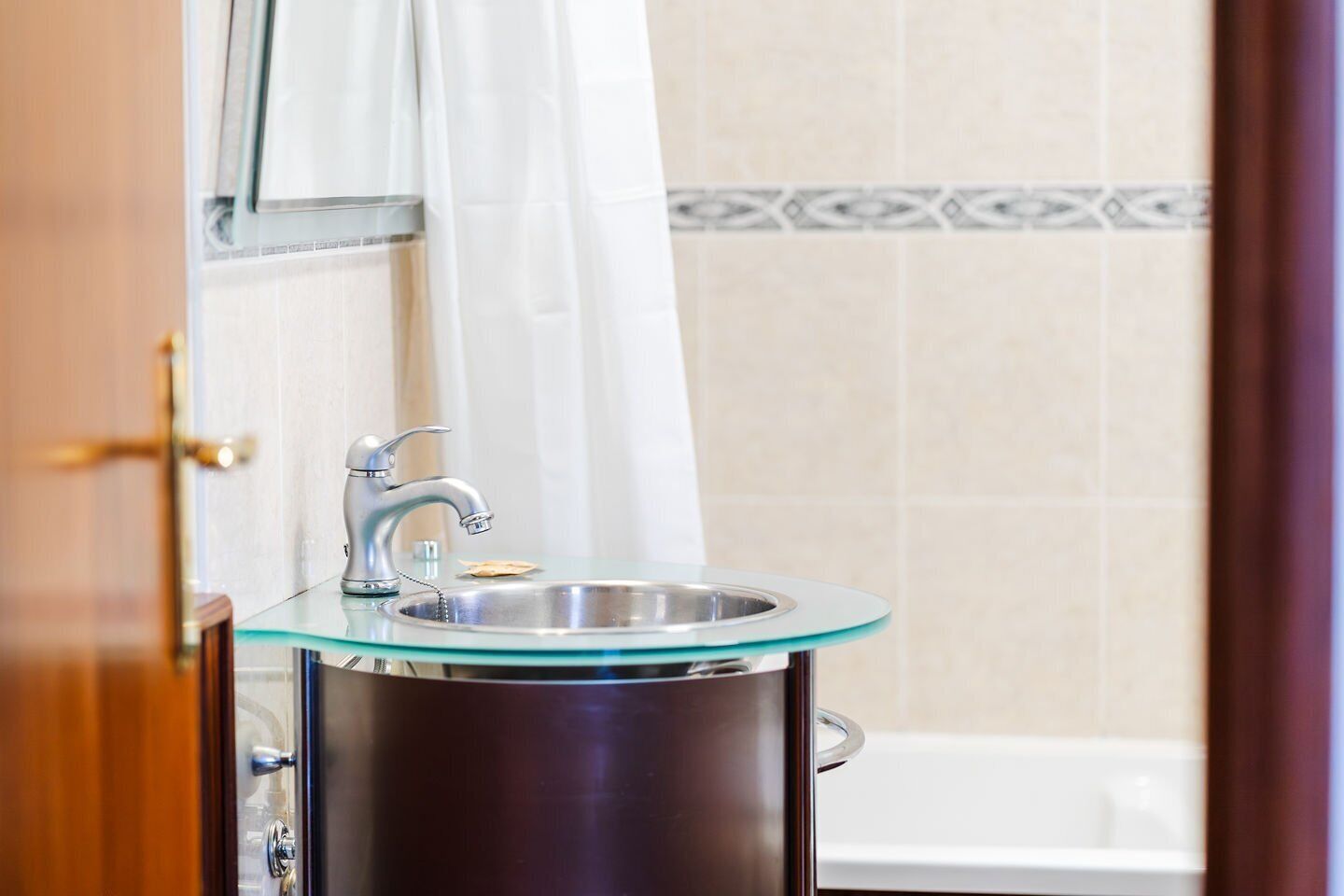 Un baño con lavamanos de vidrio, cortina de ducha y pared con azulejos.