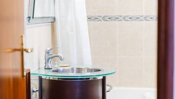 Un baño con lavamanos de vidrio, cortina de ducha y pared con azulejos.