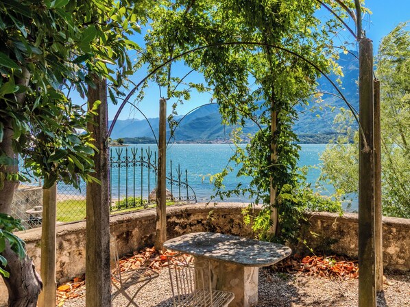 A garden with a table and chairs, surrounded by trees and a view of a lake and mountains.