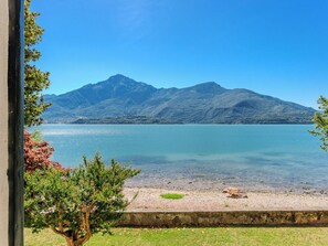 Vista despejada de un lago con montañas al fondo, una zona verde en primer plano y un sendero de piedra que lleva al agua.