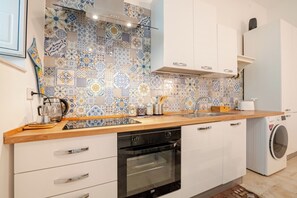 A kitchen with patterned tiles, a built-in oven, a washing machine, and white cabinetry. - A wonderful home in the historic district (Castellana Grotte)