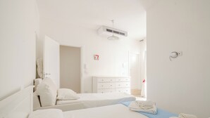 Ein Hotelzimmer mit zwei Betten, einer weißen Kommode, einem Deckenventilator und einem Fenster.
