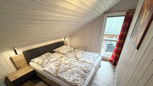 Ein Schlafzimmer mit holzverklebter Schräge, einem Bett mit floralem Bettzeug, einem kleinen Nachttisch und einem Fenster mit Vorhängen.