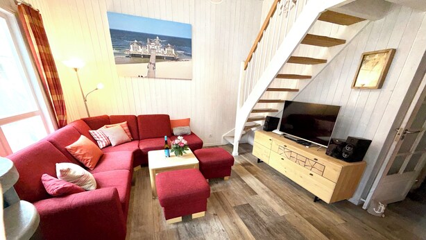 Ein Wohnzimmer mit einem roten Sofa, einem Holztisch, einem Fernseher auf einer Holzkommode und einer Treppe.