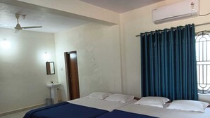 A room with two beds, a ceiling fan, an air conditioning unit, a window with curtains, and a small sink. - Stone Wood Stay (Bhatkal)