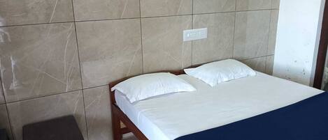 Una cama individual con ropa de cama blanca en una habitación con paredes de baldosas.