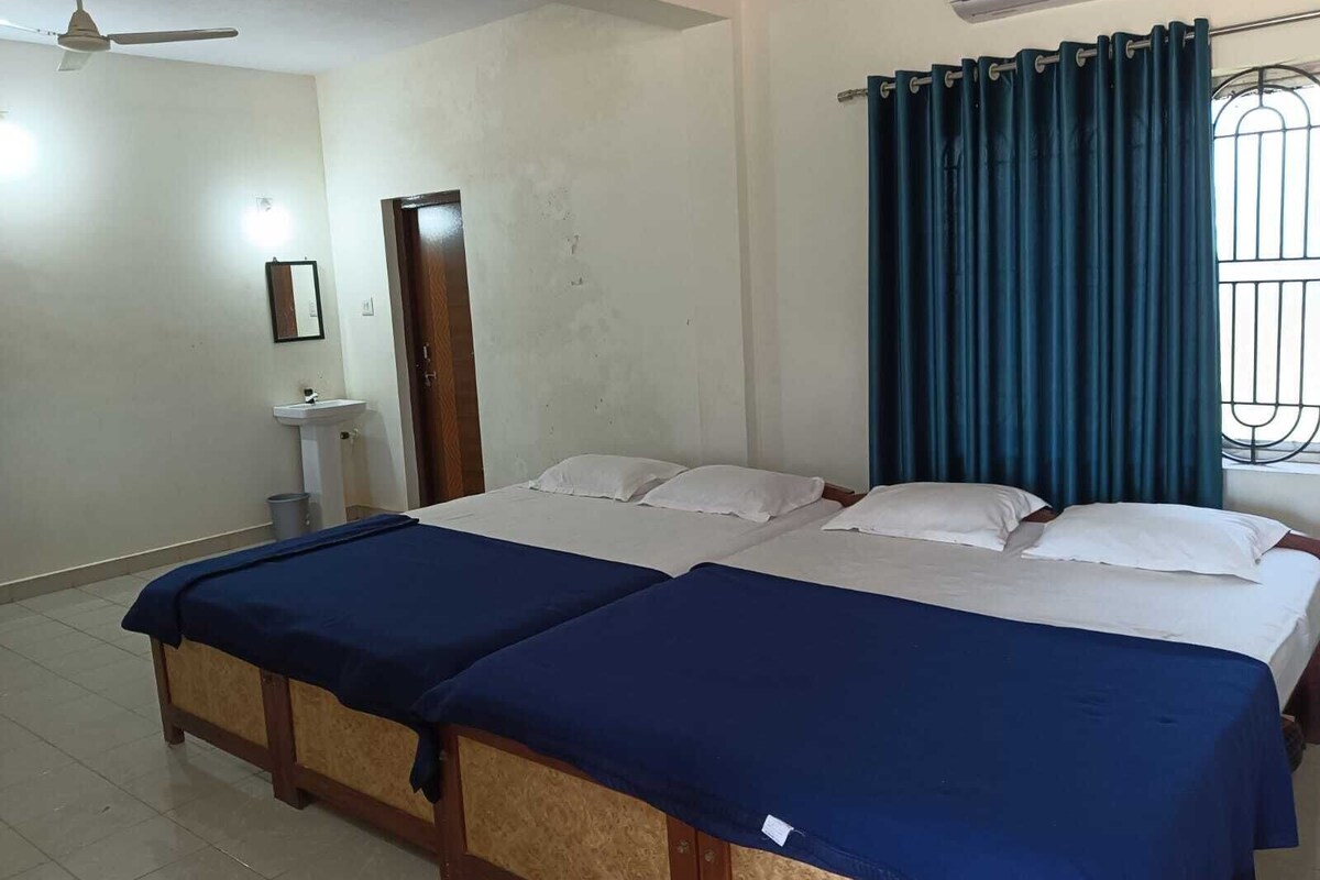 A room with two beds, a ceiling fan, a window with curtains, a sink, and an air conditioning unit.