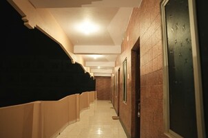 Un pasillo con suelo de baldosas, techo con iluminación empotrada y una puerta a la derecha.