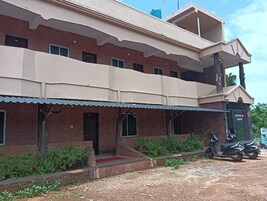 Un edificio de dos plantas con techo plano, un balcón en el piso superior y una zona de entrada cubierta.