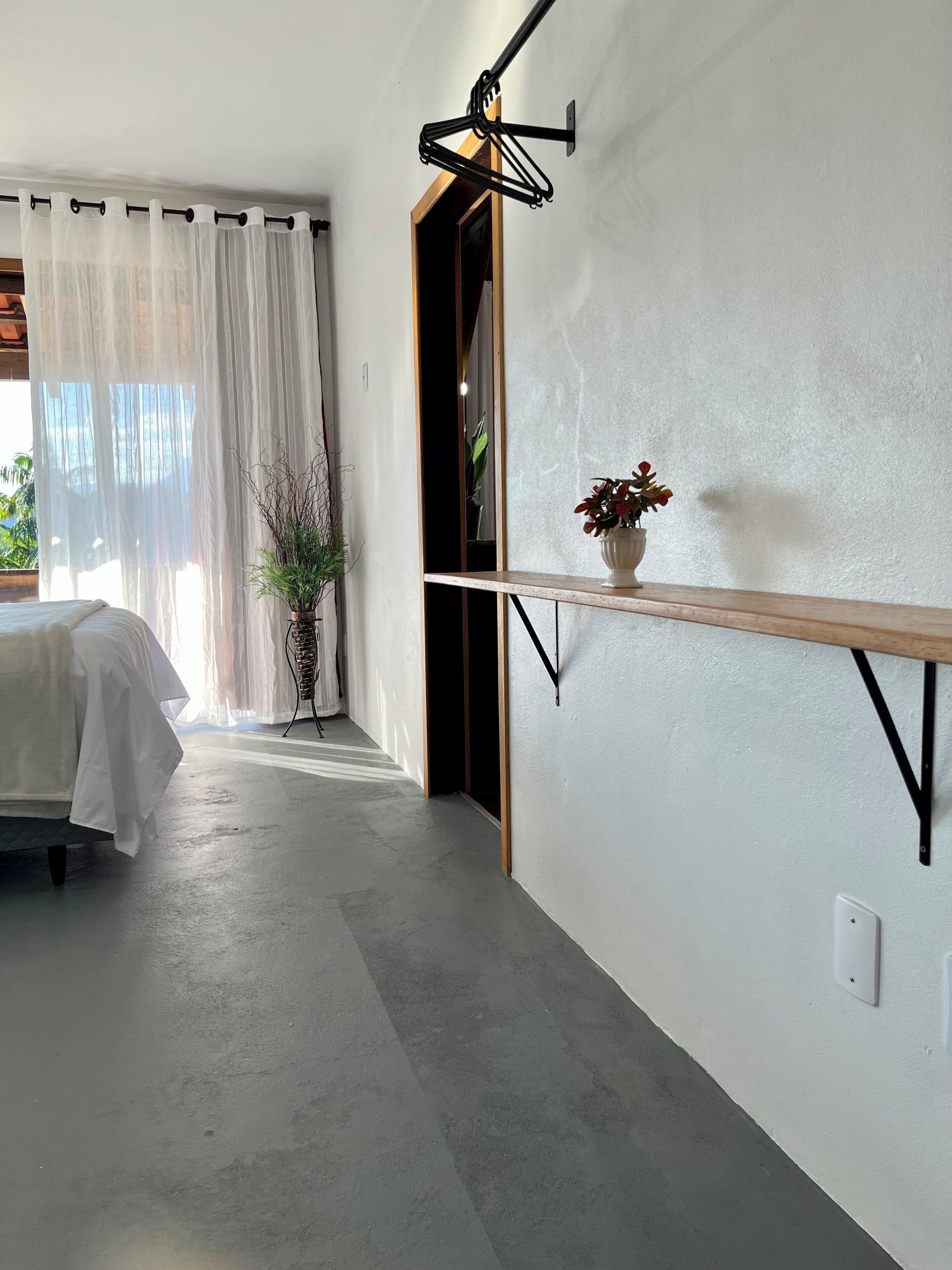 Een moderne kamer met een bed, een potplant, een plank en een wandlamp.