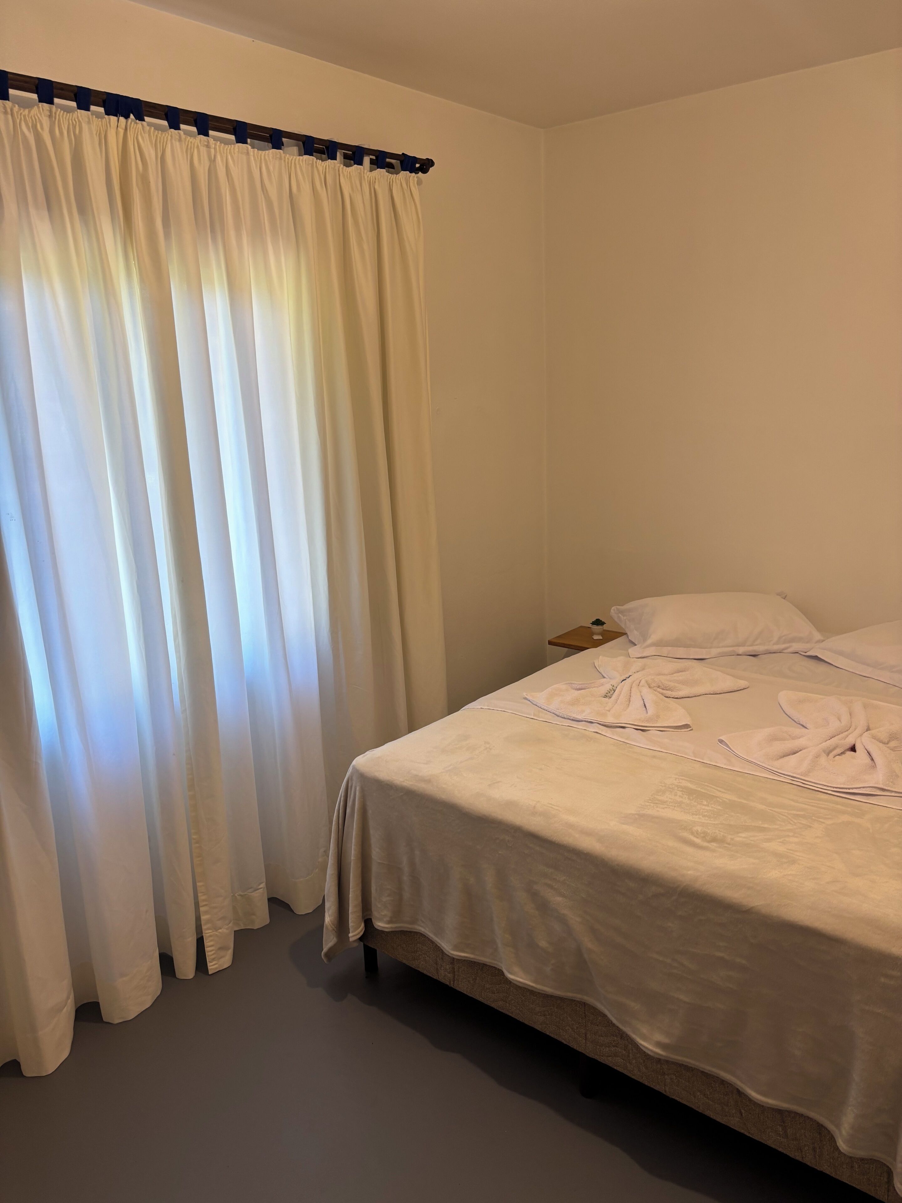 Un dormitorio con cama, cortinas blancas y cabecera de madera.