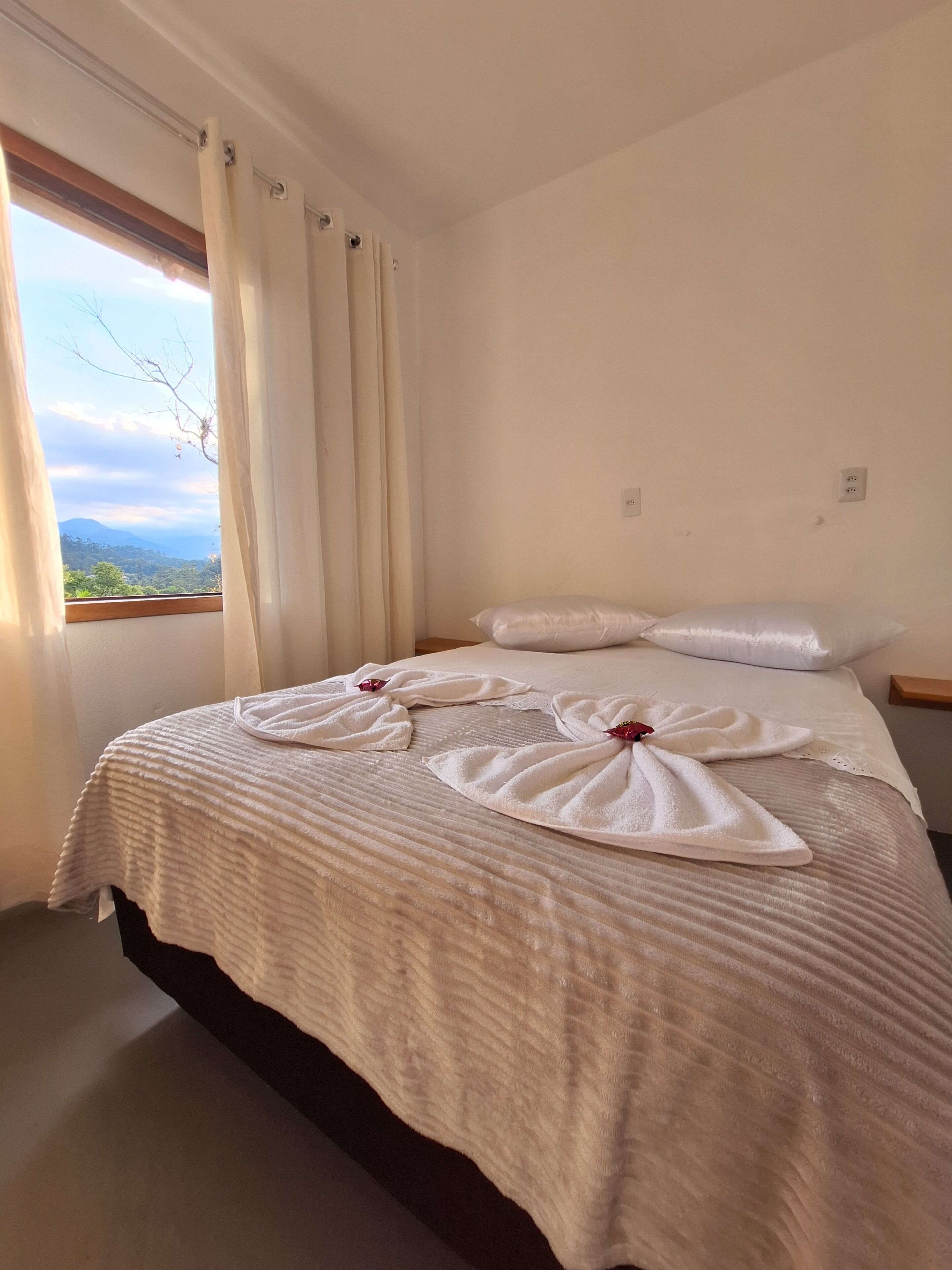 Habitación de hotel con cama, cortinas, una ventana y toma de corriente.