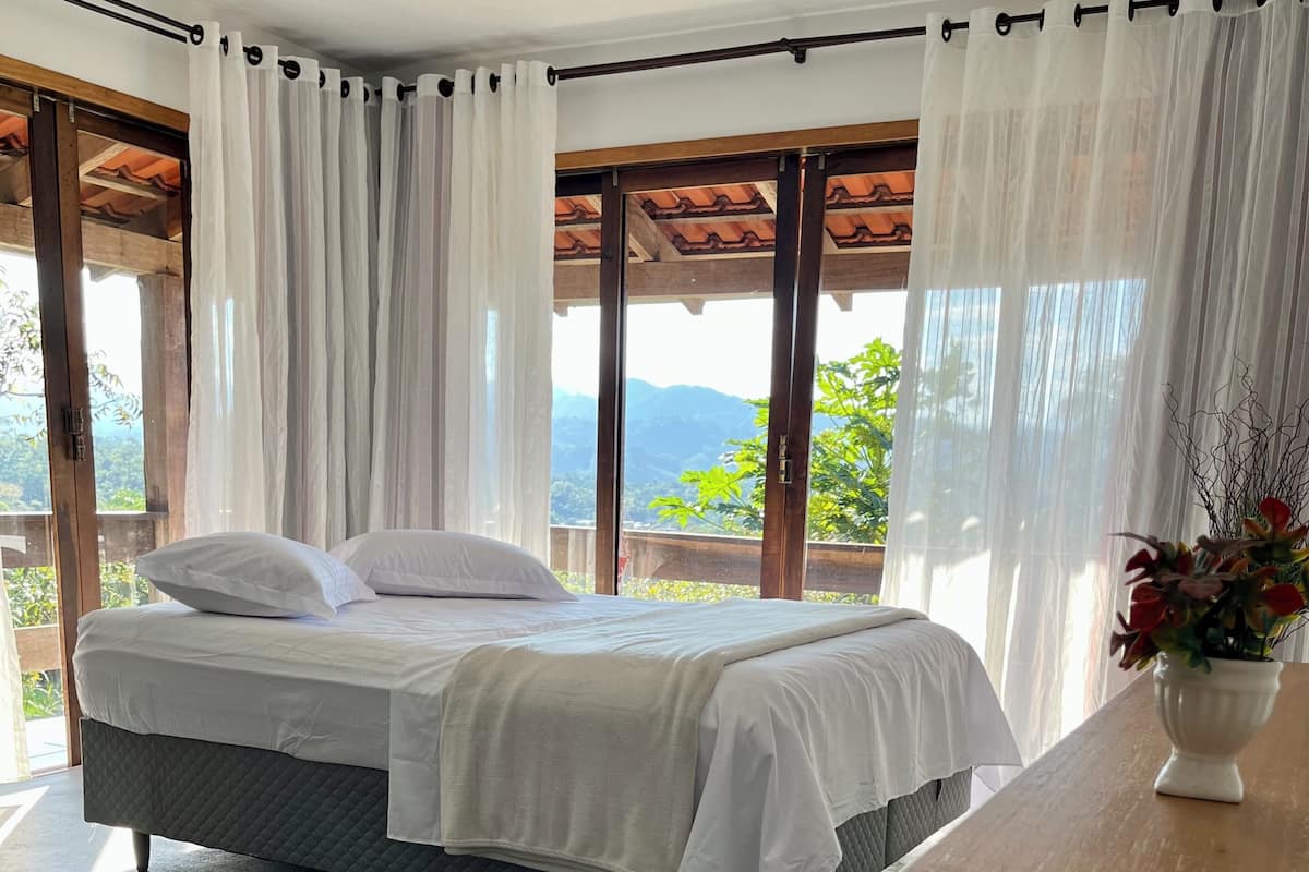 Un dormitorio con una cama, una mesa de madera y vistas a montañas a través de ventanas amplias.