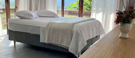 A bedroom with a bed, a wooden table, and a view of mountains through large windows.