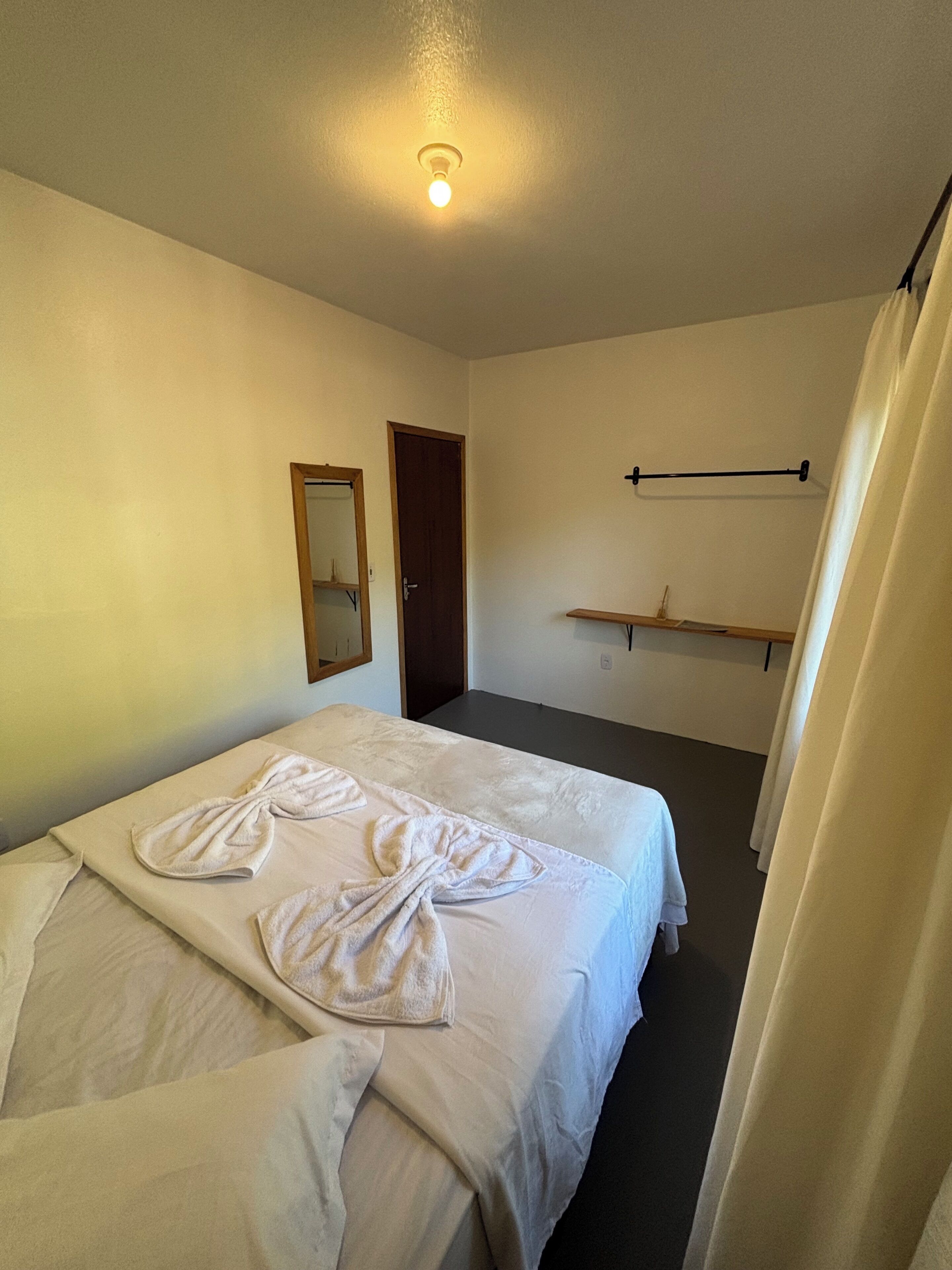 Une chambre d’hôtel avec un lit, un miroir, une porte, un porte-serviettes et un rideau.