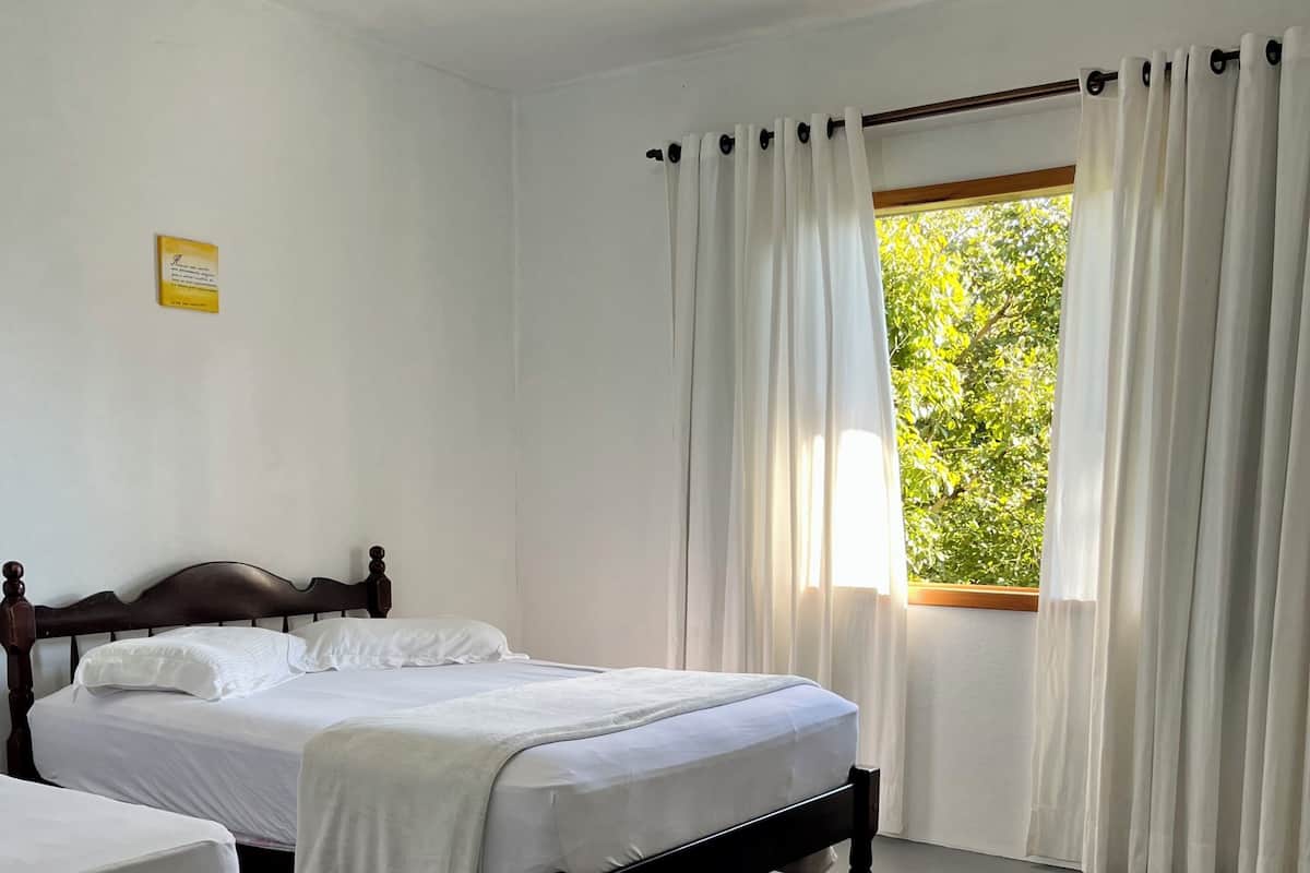 Un dormitorio con cama, mesita de noche y ventana con cortinas.