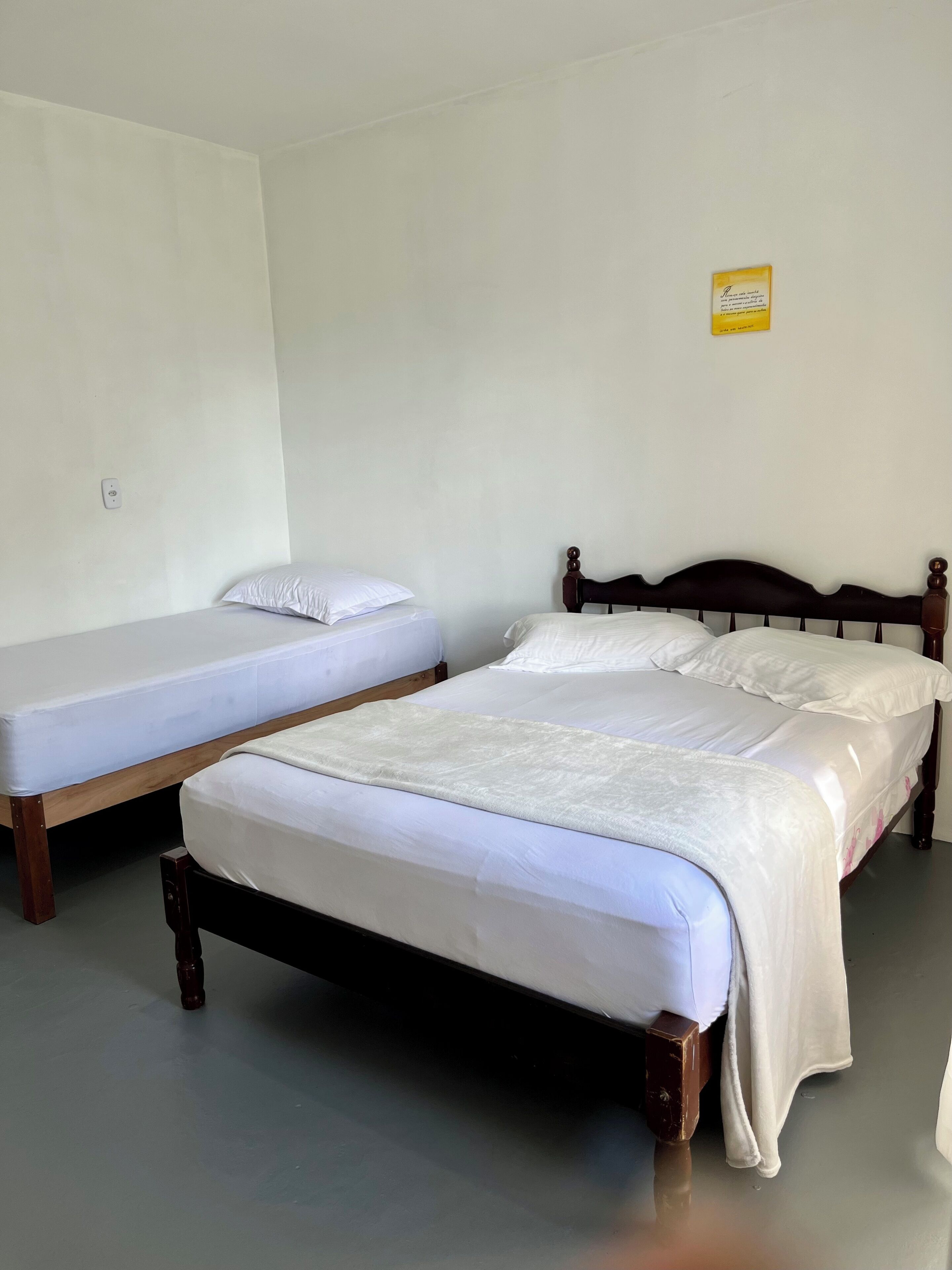 Two single beds with wooden frames in a room with plain white walls and a grey floor.