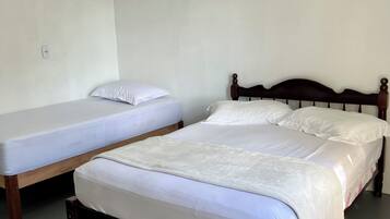 Two single beds with wooden frames in a room with plain white walls and a grey floor.