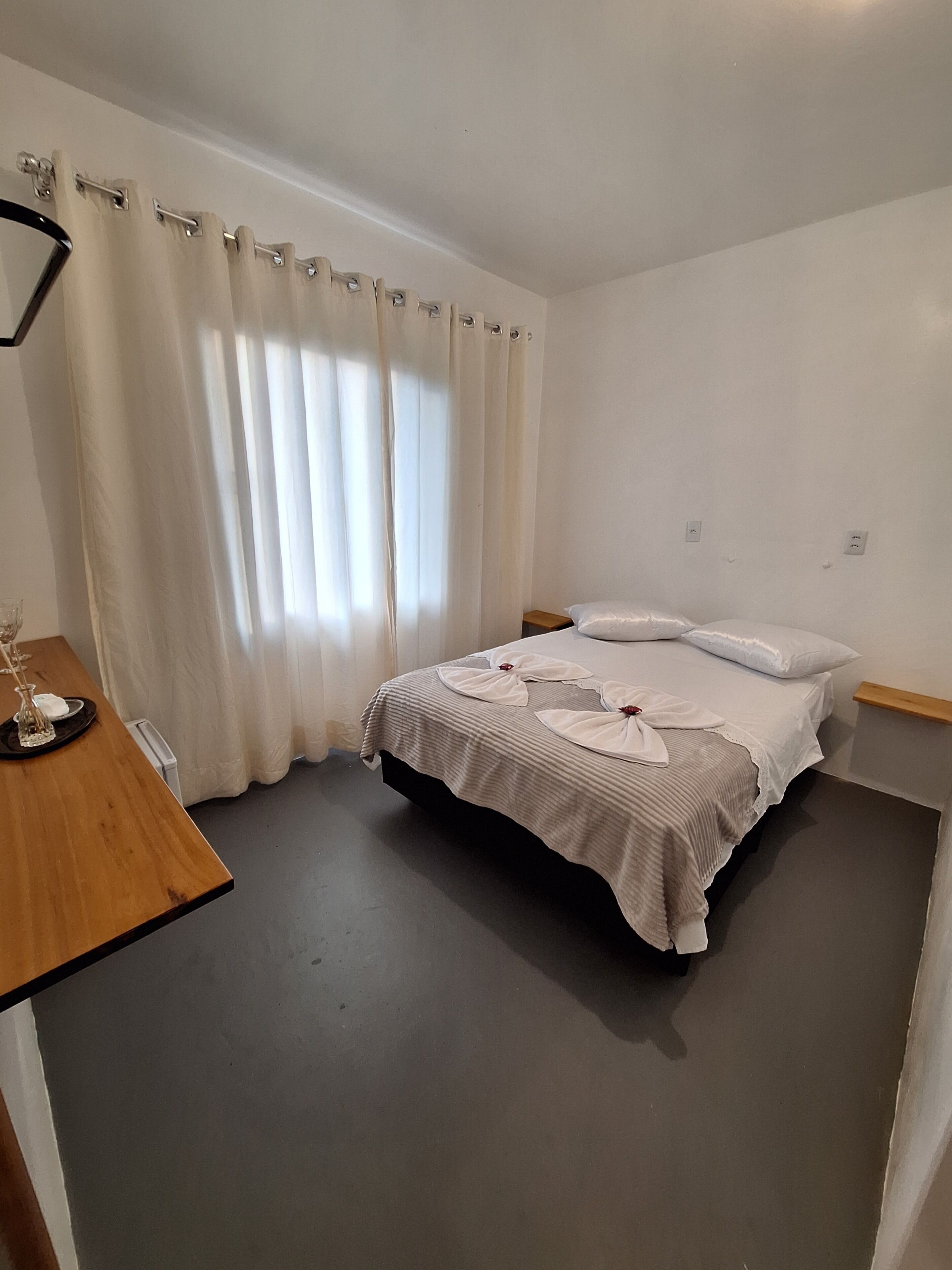 Un dormitorio con cama, cortinas, mesita de noche y escritorio de madera.