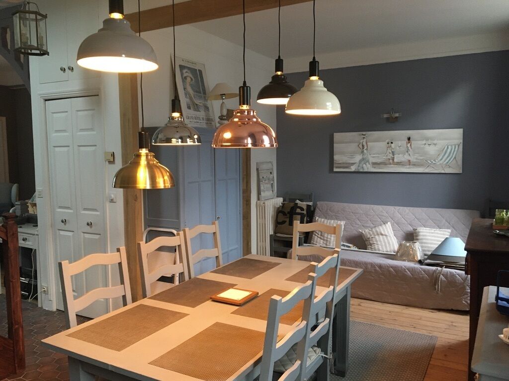 Un espace repas comprenant une table, des chaises, des luminaires suspendus et un tableau au mur.