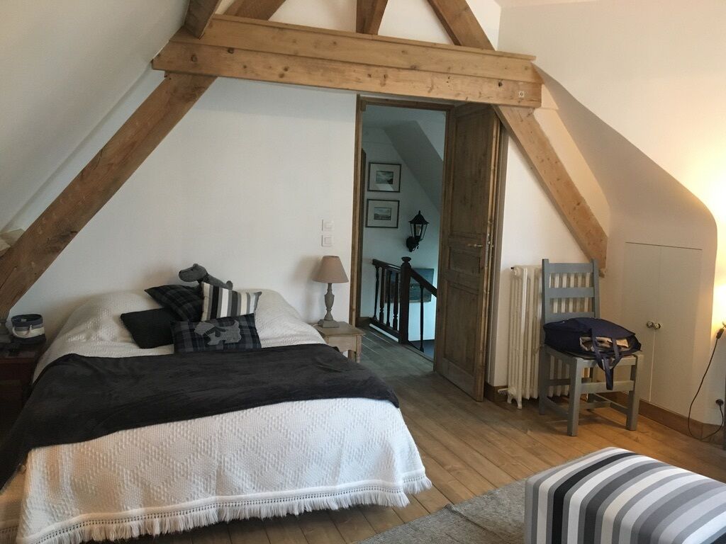 Une chambre avec un plafond en pente, un lit recouvert d’une couvre-lit noire et blanche, une chaise et un radiateur.