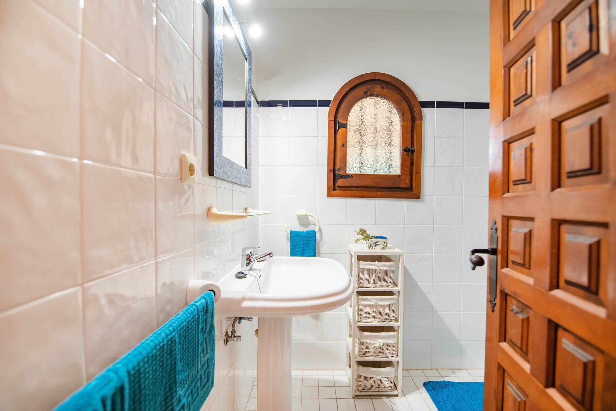 A bathroom with a white sink, a blue towel, a wooden door, and a window with a decorative frame.