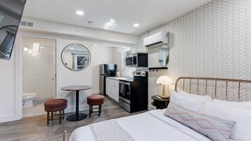 Une chambre d’hôtel moderne équipée d’un lit, d’une petite kitchenette, d’un miroir rond et d’une salle de bain avec des toilettes et un lavabo.
