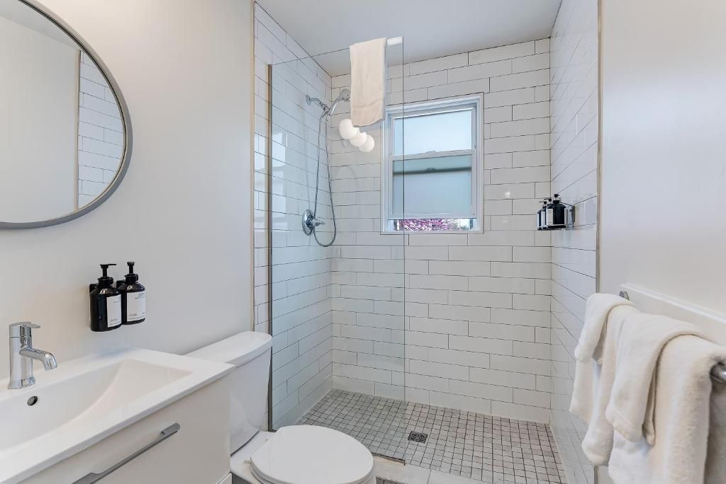 A modern bathroom with a white sink, toilet, and shower. There is a window with a view of the outside.