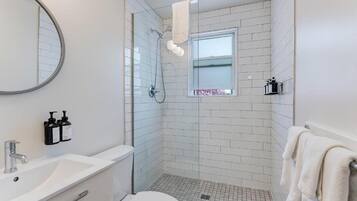 Une salle de bain moderne avec un lavabo, des toilettes et une douche, le tout de couleur blanche. Une fenêtre offre une vue sur l’extérieur.