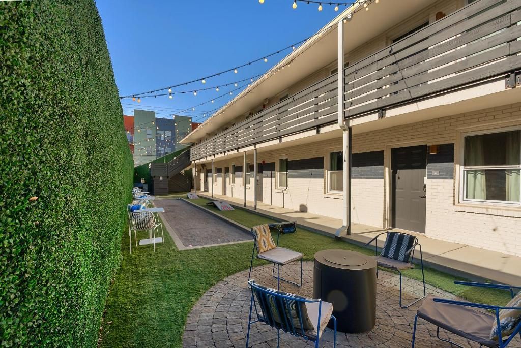 An outdoor seating area with chairs and a table, surrounded by a neatly trimmed hedge and a building with a flat roof.