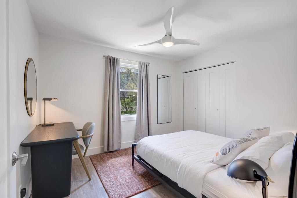 A bedroom with a bed, a desk, a chair, a ceiling fan, and a window with curtains.