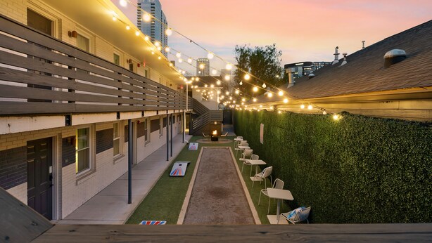 Un patio con seto verde, mobiliario exterior e iluminacion con guirnaldas.