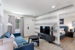 A modern living room with a sofa, a TV, a small table, and a bed. - State Street (Nashville)