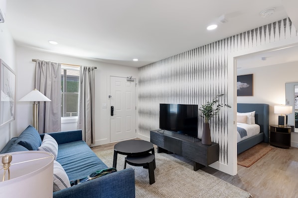 A modern living room with a sofa, a TV, a small table, and a bed. - State Street (Nashville)