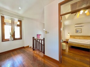 A hotel room with wooden flooring, a bed, a window with curtains, a painting on the wall, and a ceiling fan. - The Midas Pool Villa (Banglamung)