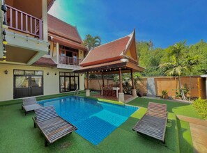 A swimming pool with lounge chairs, a covered seating area, and a two-story building with a balcony. - The Midas Pool Villa (Banglamung)