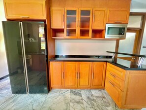A kitchen with wooden cabinets, a black refrigerator, a microwave, and a marble floor. - The Midas Pool Villa (Banglamung)