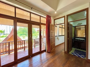 A room with large sliding glass doors leading to a balcony, a wooden floor, and a bathroom with a sink and mirror. - The Midas Pool Villa (Banglamung)