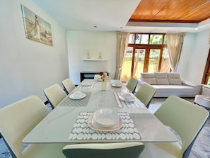 A dining area with a glass table, chairs, and a sofa in the background. - The Midas Pool Villa (Banglamung)