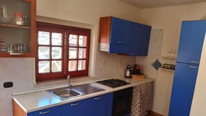 A kitchen with blue cabinets, a stainless steel sink, a window, and a tiled backsplash.