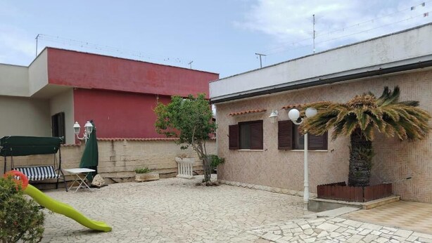 A courtyard with a red building, a palm tree, outdoor furniture, and a lamp post.