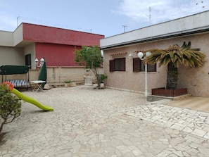 Une cour avec un sol carrelé, un palmier, un parasol vert et un bâtiment rouge.
