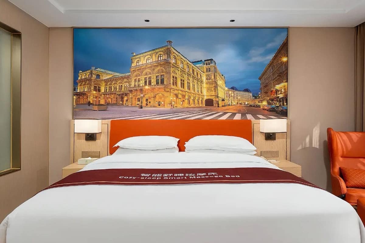 Quarto de hotel com uma cama grande, um mural da paisagem urbana na parede e uma poltrona de couro.