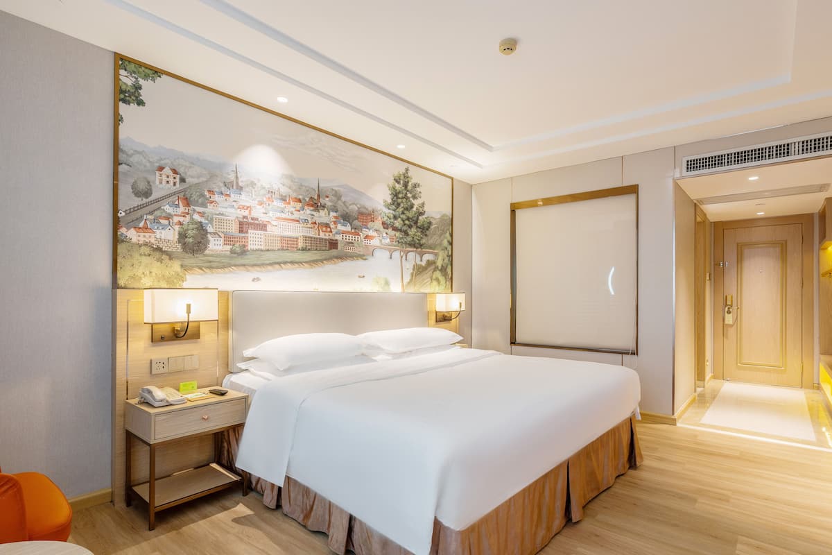 Quarto de hotel com cama, mesas de cabeceira, um quadro e uma porta.